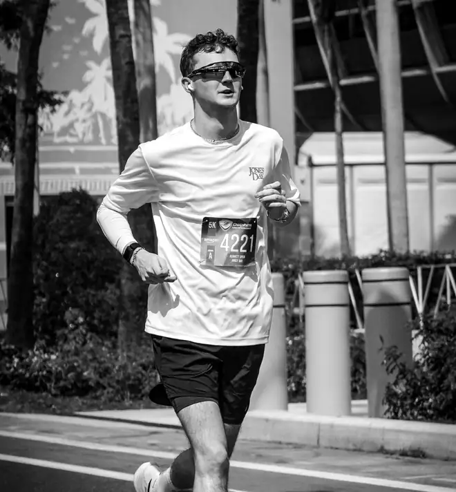 A runner wearing sunglasses and a race bib on a city street