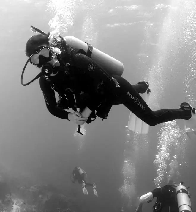 A scuba diver swimming above a reef, with other divers below